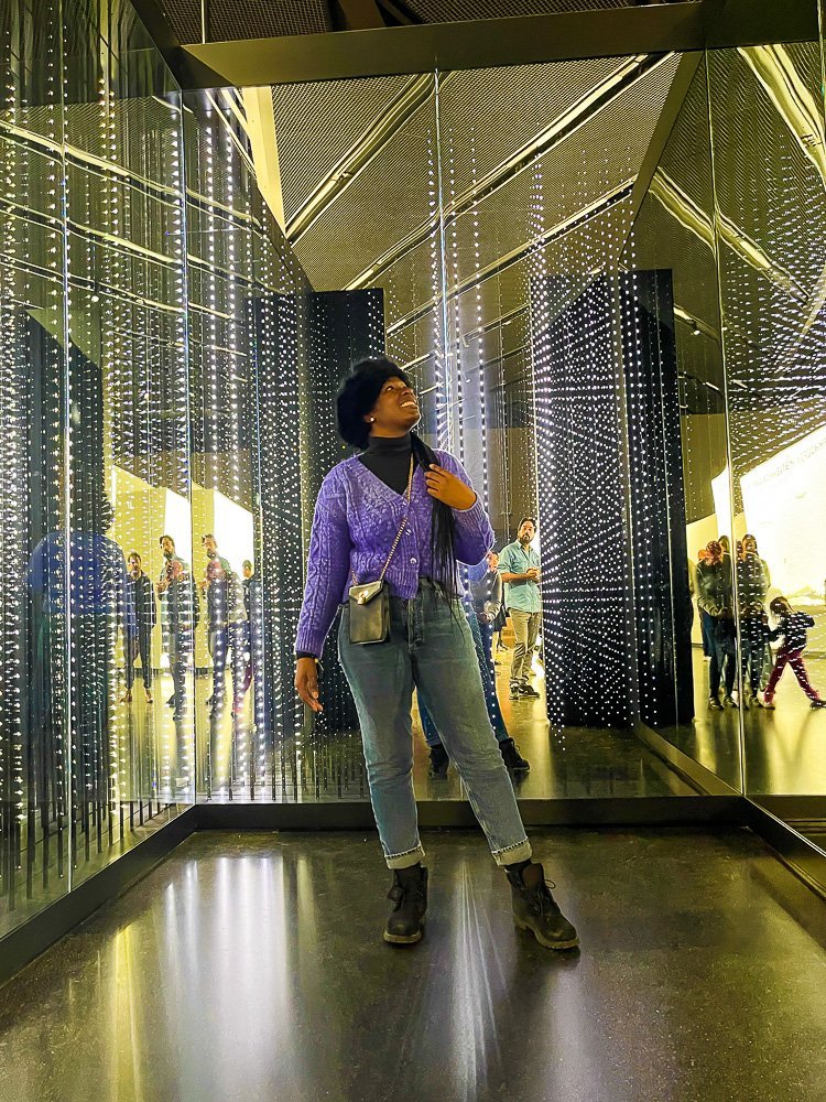 Jazzmine wearing a chunky purple cardigan and posing inside light display at Futurium Berlin.