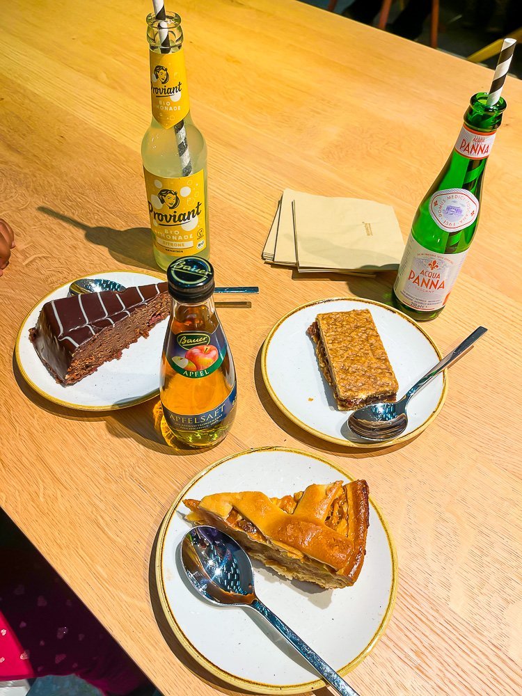 plated slices of pie and chocolate cake with bottled juices on a wooden table.