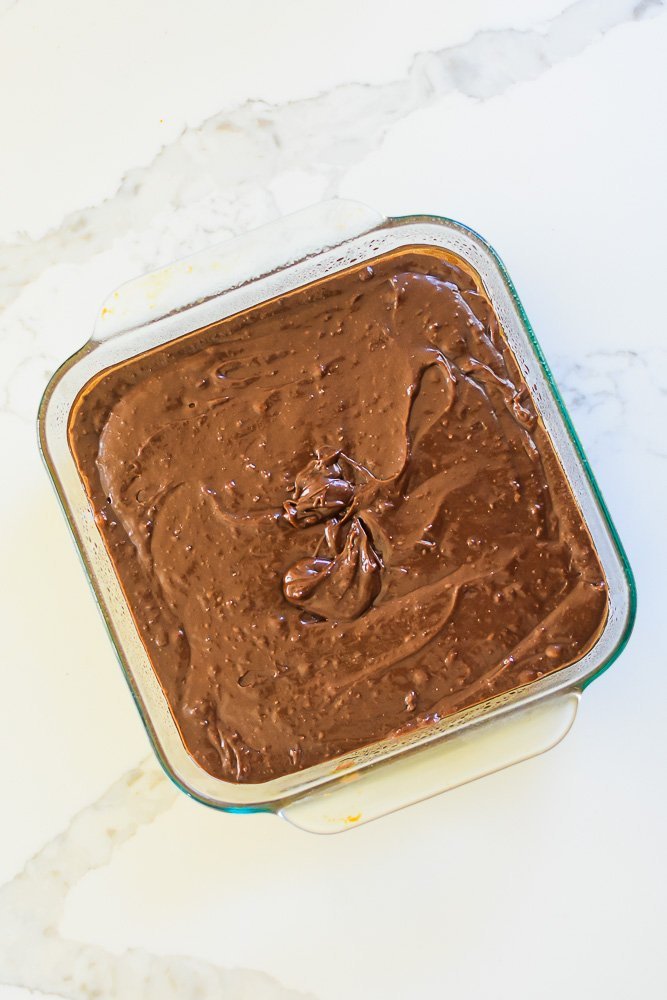 brownie batter in square glass pan.