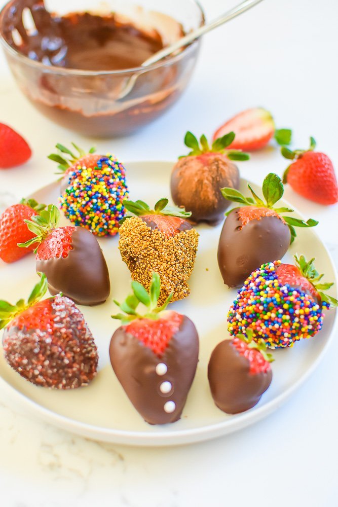 platter of decorated chocolate dipped strawberries with bowl of melted chocolate in background.
