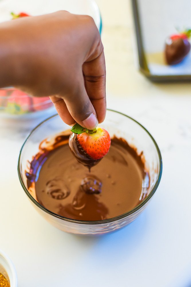 lifting strawberry out of bowl of melted chocolate.