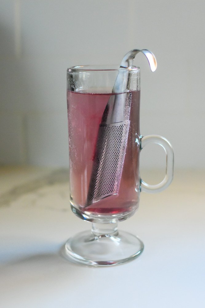 loose hibiscus tea in metal strainer steeping in hot water.