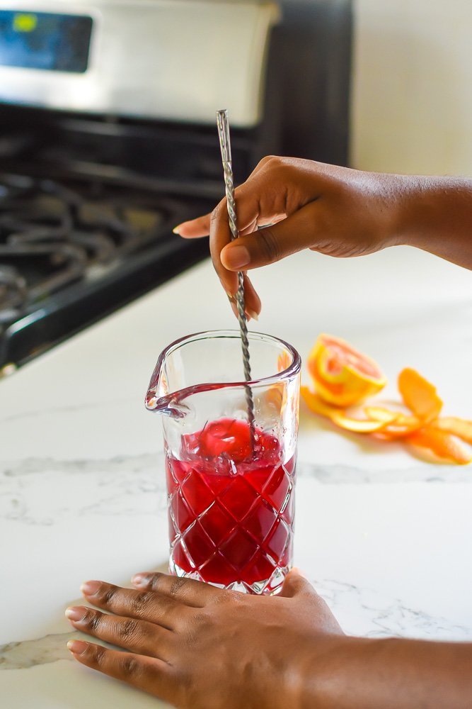 mixing hibiscus mocktail over ice with bar spoon.