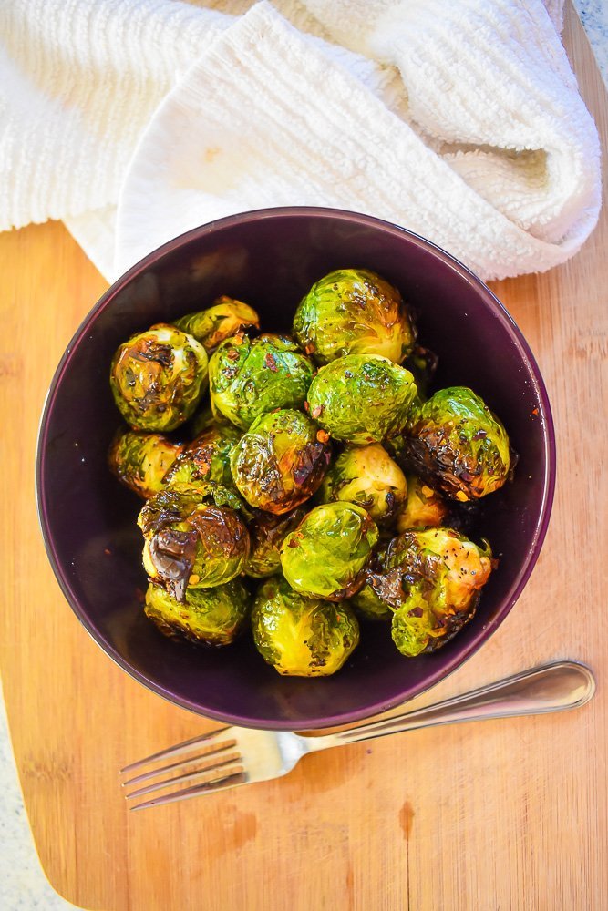 crispy roasted brussels sprouts in a purple bowl on a wooden cutting board.