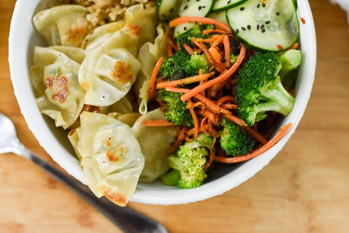 mini chicken and vegetable wontons, quick pickled cucumber slices, and sauteed broccoli and carrot in white bowl.
