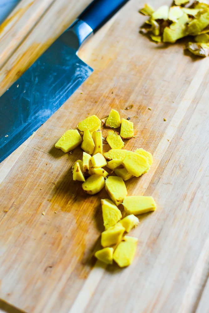 peeled and sliced ginger on wooden cutting board with knife.