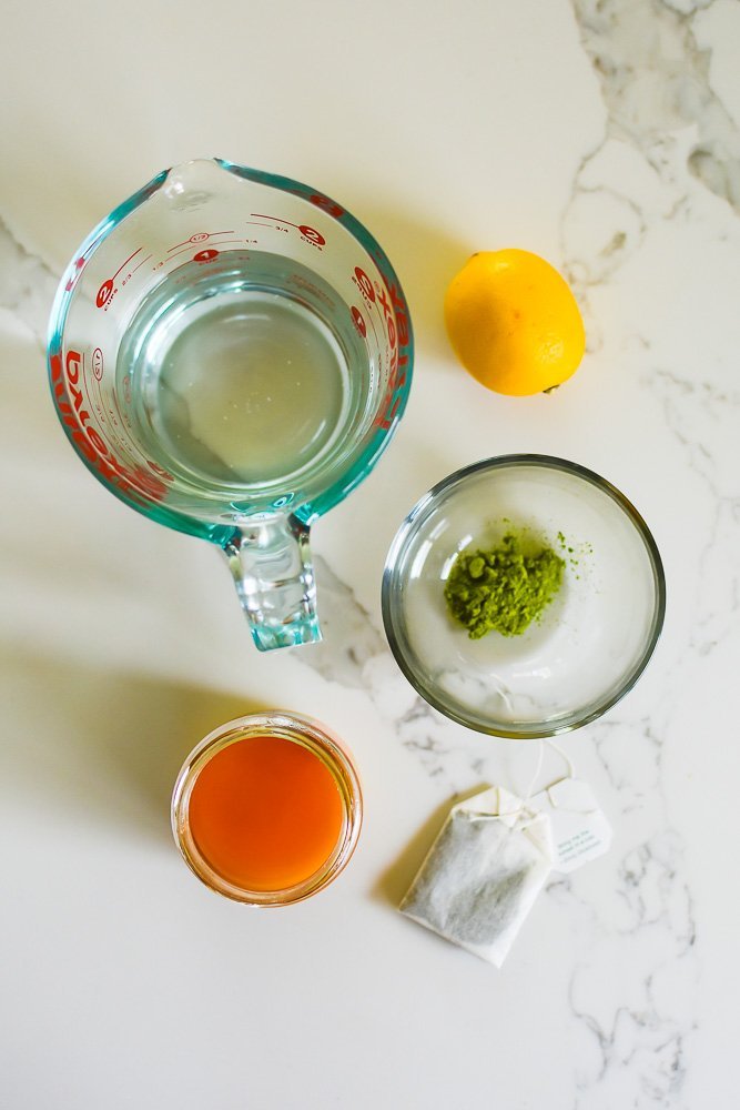 hot water, fresh lemon, matcha powder, honey, and spearmint tea bag on granite counter top.
