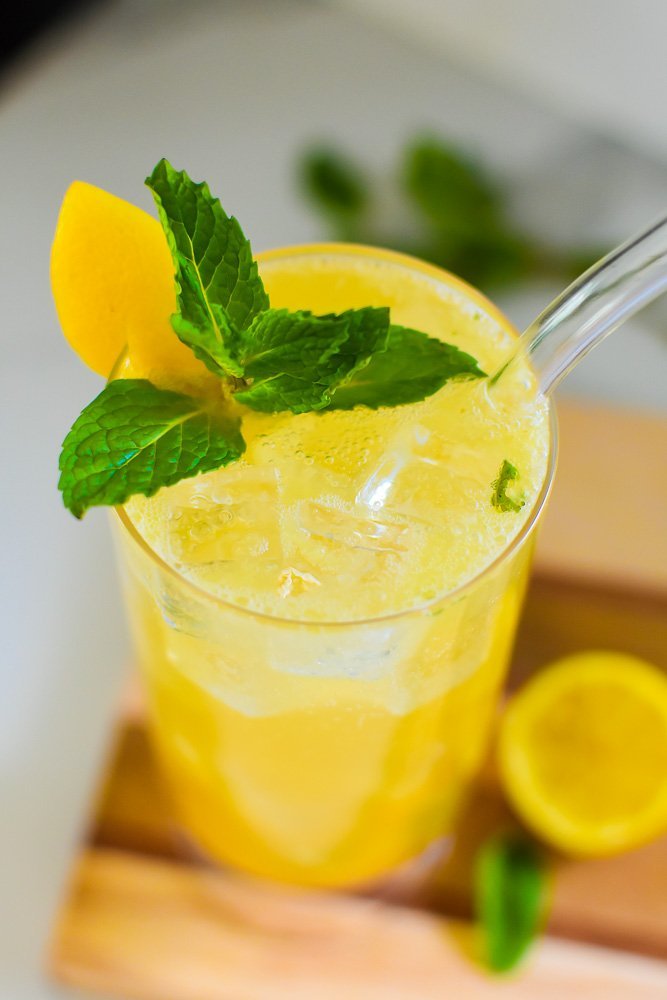 fizzy mint mocktail with glass straw and fresh lemon and mint garnishes.