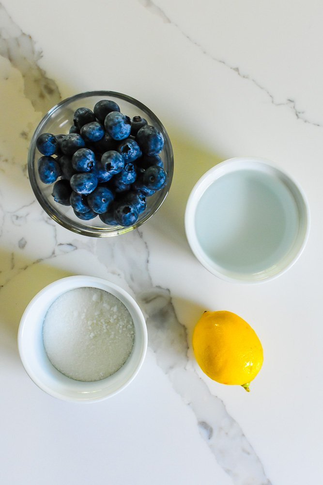 fresh blueberries, lemon, granulated sugar, and water on granite counter top.