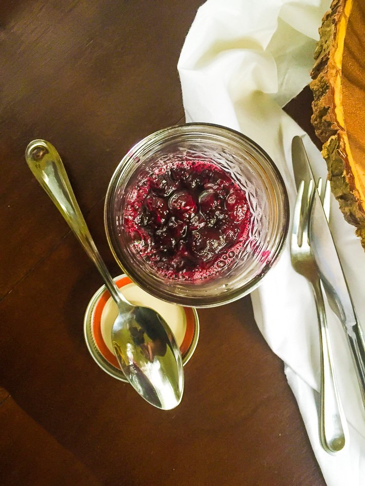 jar of fresh blueberry compote on wooden tabletop next to silver tablespoon.