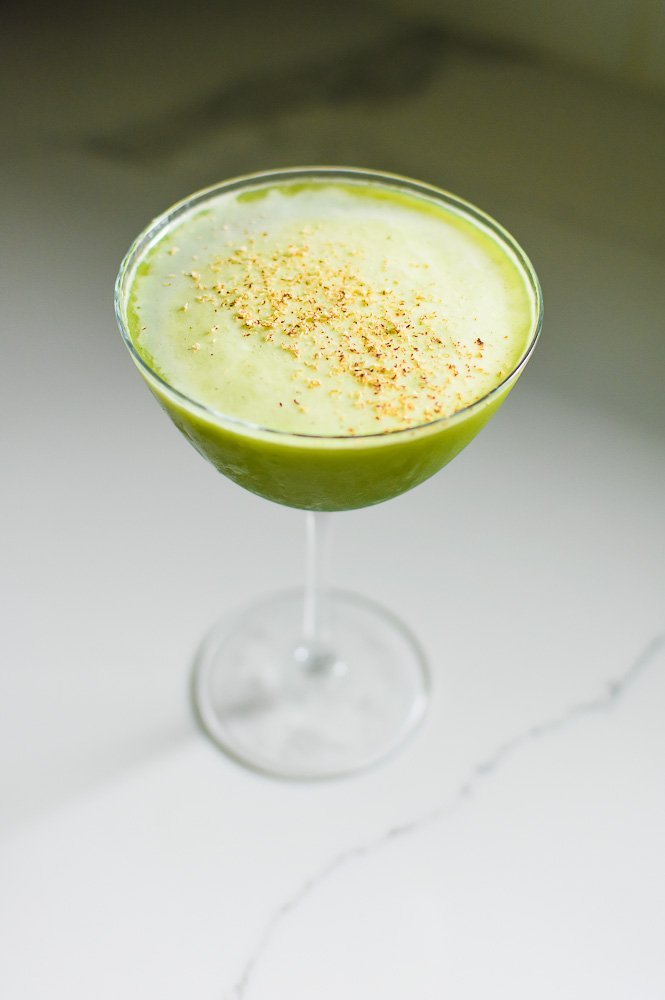 green matcha martini in cold glass garnished with freshly shaved nutmeg on granite countertop.