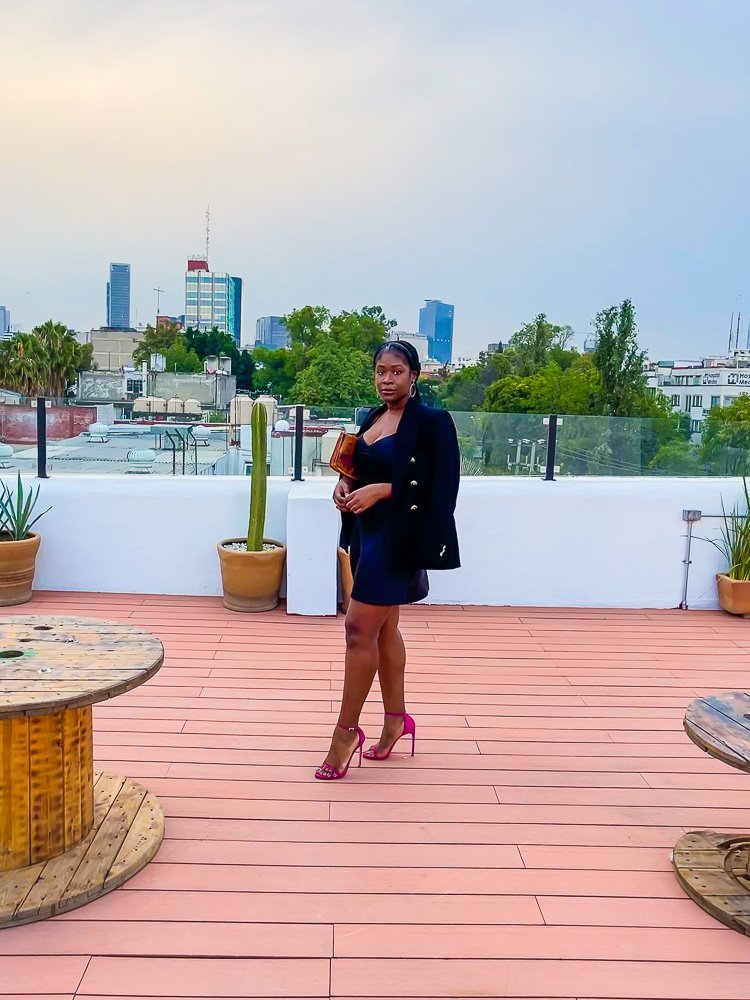 Jazzmine posing on rooftop at sunset in all black dinner outfit with pink shoes.