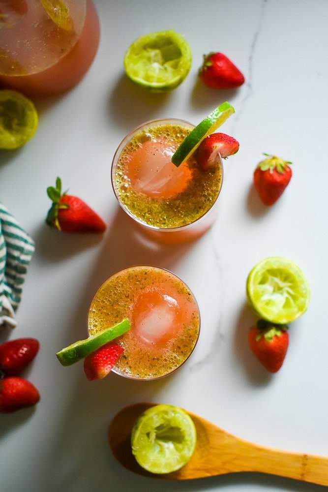 two glasses of strawberry limeade with fresh mint surrounded by fresh strawberries and juiced limes.