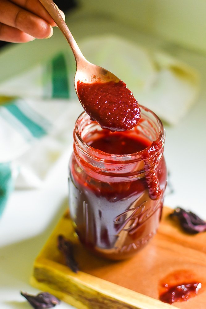 spooning hibiscus barbecue sauce out of mason jar with sauce dripping down side of jar.