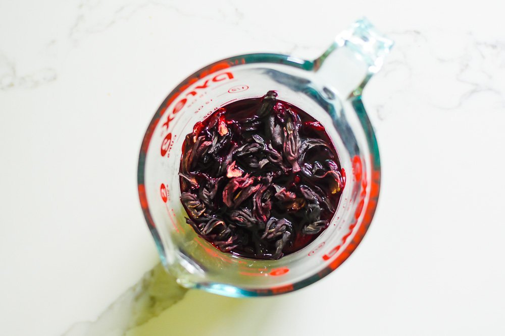 steeped hibiscus petals in glass measuring cup.