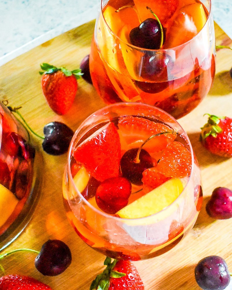 two glasses of rosé wine sangria with cherries, strawberries, and peaches.