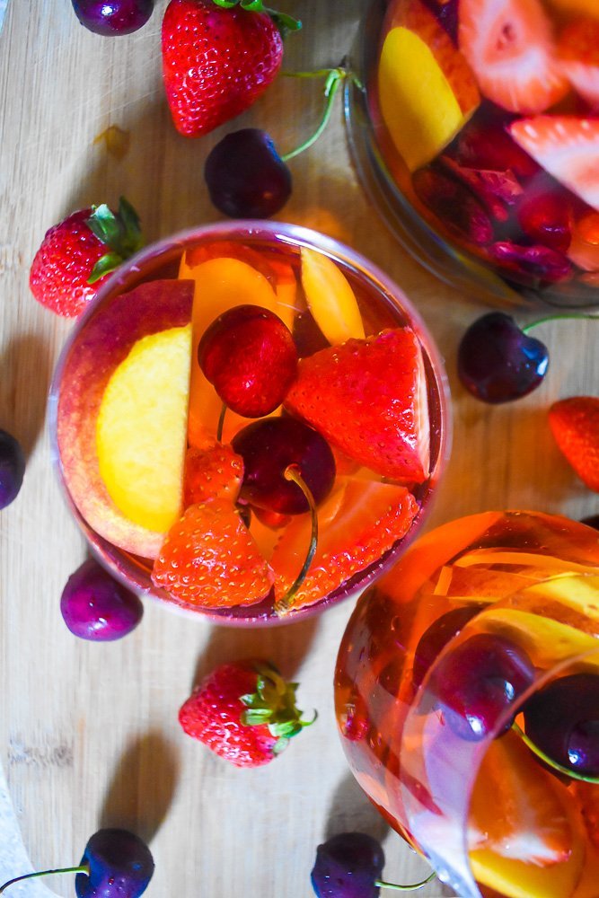 pink rosé sangria on cutting board surrounded by fresh cherries and strawberries.