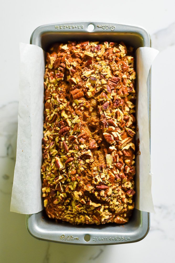 freshly baked loaf of homemade banana bread with crunchy pecan topping in loaf pan.