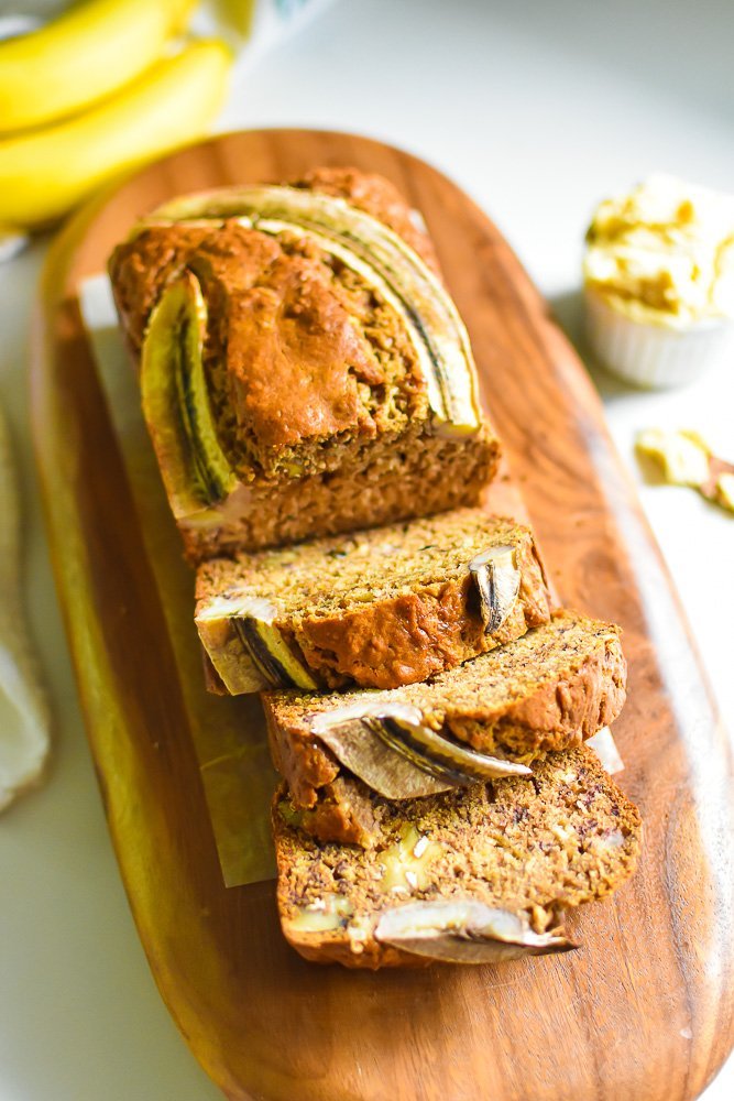 loaf of chai spiced banana bread with three pieces sliced on wooden cutting board.