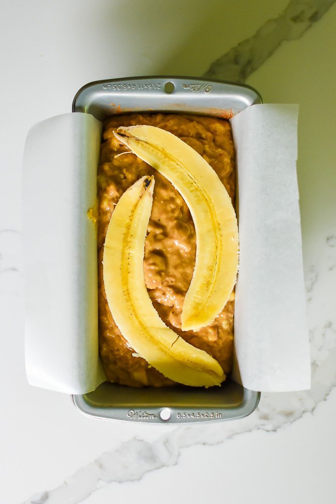 banana chai bread batter in loaf pan with split banana on top.
