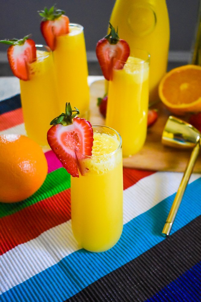 stemless champagne flute of tequila mimosa surrounded by fresh oranges and strawberries.