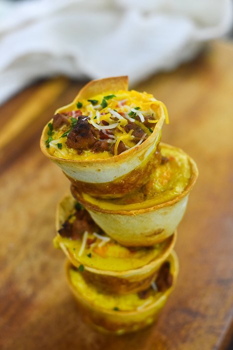 four tortilla wrapped baked egg cups stacked on wooden cutting board.