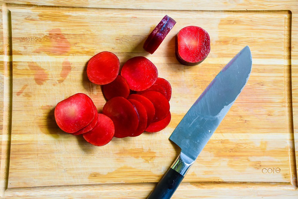 sliced red plums on wooden cutting board with knife.