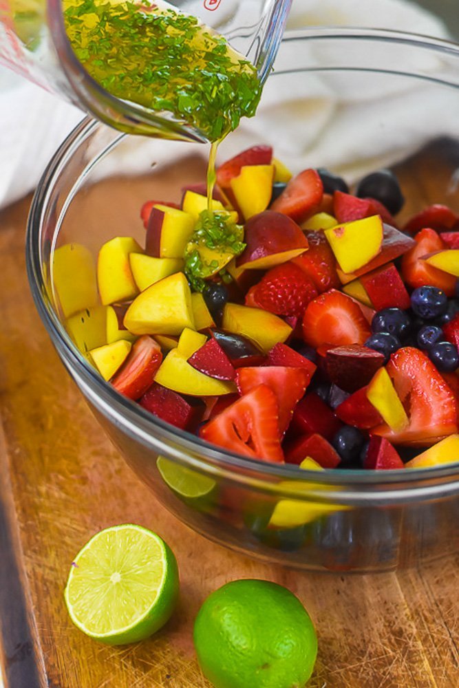 pouring honey lime mint dressing over cut summer fruits.