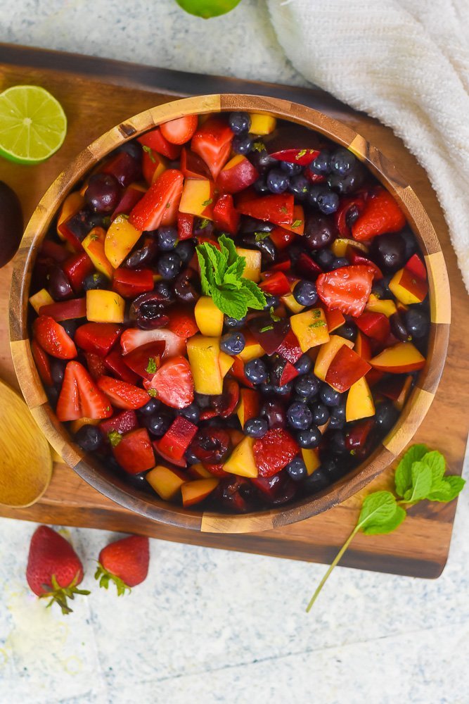 wooden bowl of fruit salad dressed in minty dressing and garnished with sprig of fresh mint.