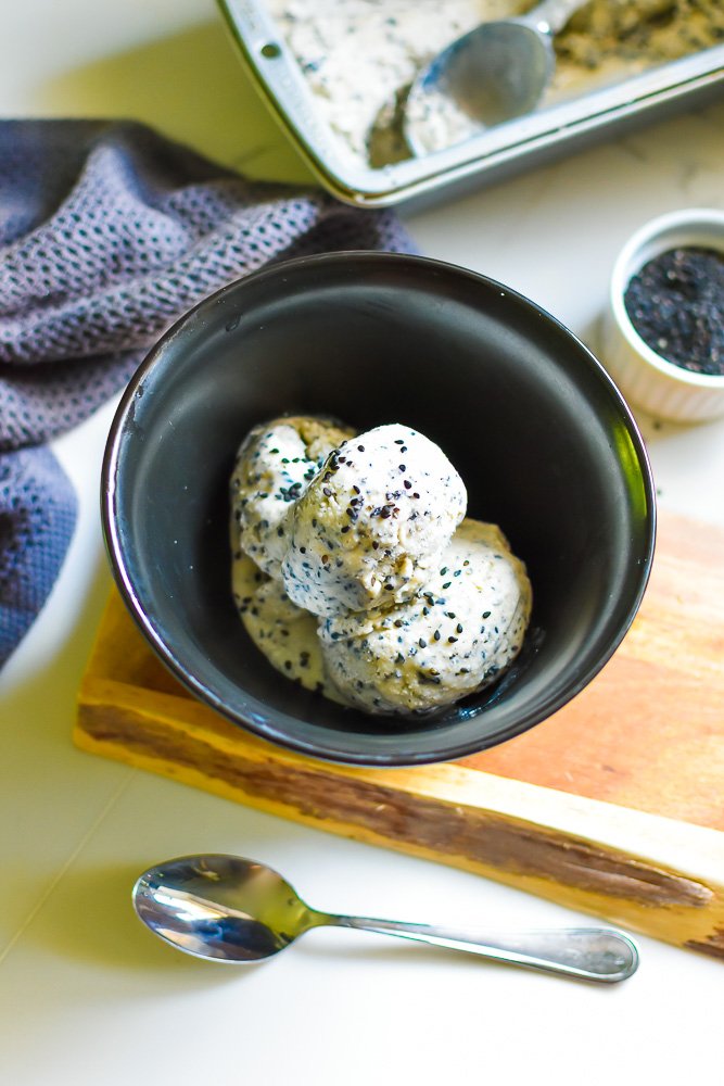 black sesame seed ice cream garnished with sesame seeds in black bowl.