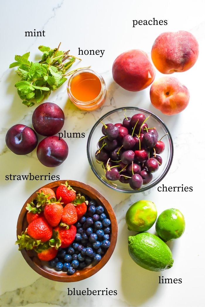 jar of honey, and fresh mint, peaches, plums, cherries, strawberries, blueberries, limes on granite countertop.