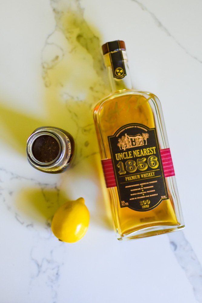 fresh lemon, bottles of brown sugar simple syrup and Uncle Nearest 1856 Whiskey on granite counter top.