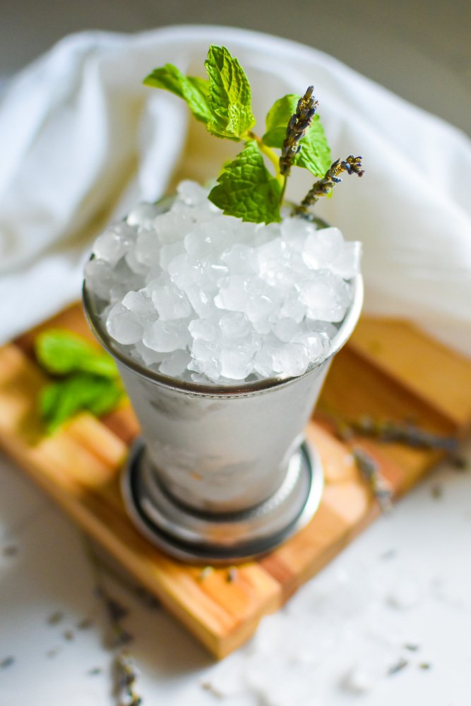 traditional mint julep cocktail presentation in silver cup with dome of crushed ice and herb garnishes.