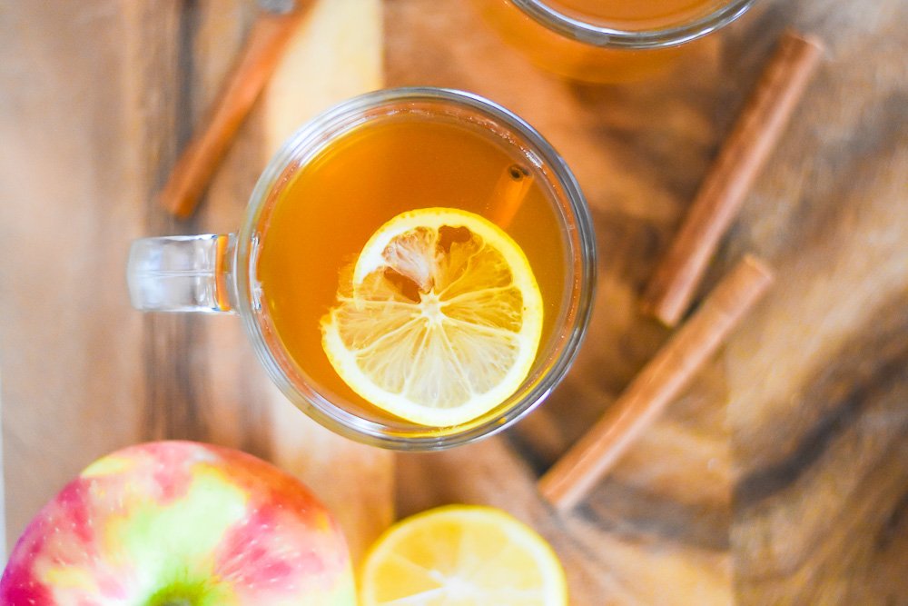 the best apple cider hot toddy next to fresh apples, lemon, and cinnamon sticks.