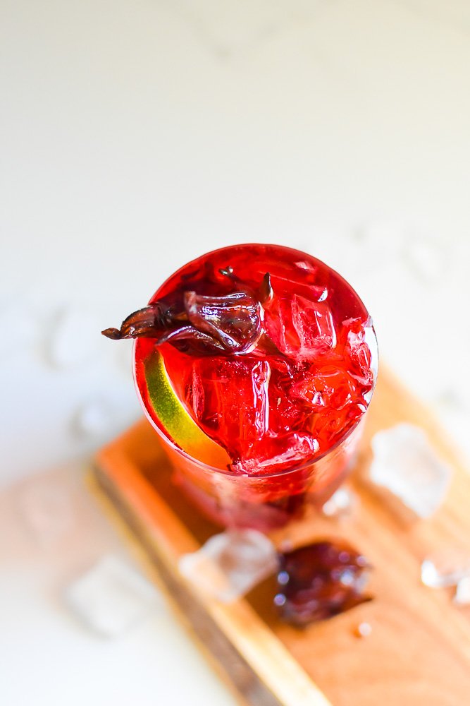 deep purple-red hibiscus gin drink with candied hibiscus flower and wheel of lime floating on top.