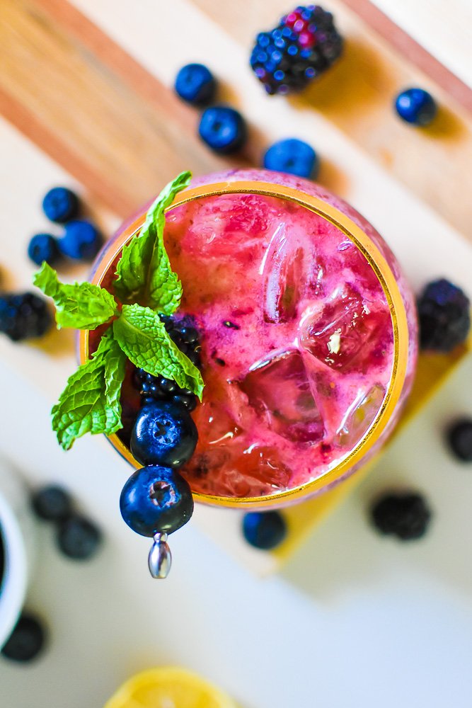 Mixed berry bourbon smash cocktail with champagne garnished with sprig of mint leaves and fresh berries on pick.
