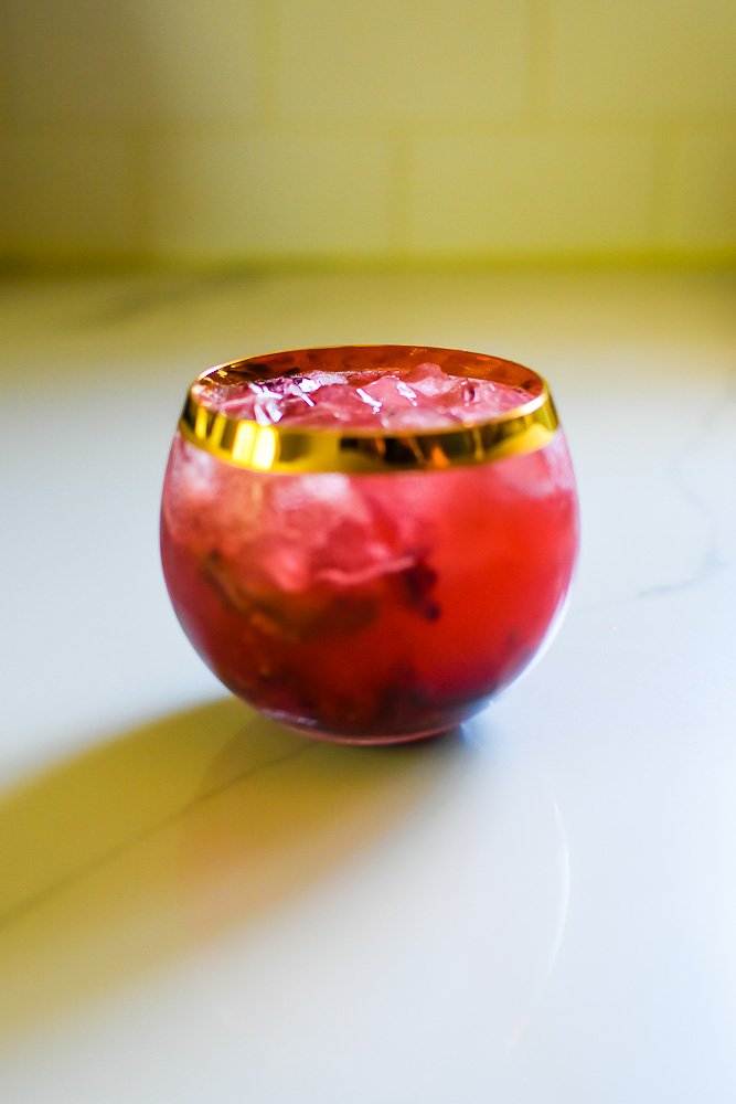 mixed berry bourbon smash mixture, ice, and champagne in rounded rocks glass.