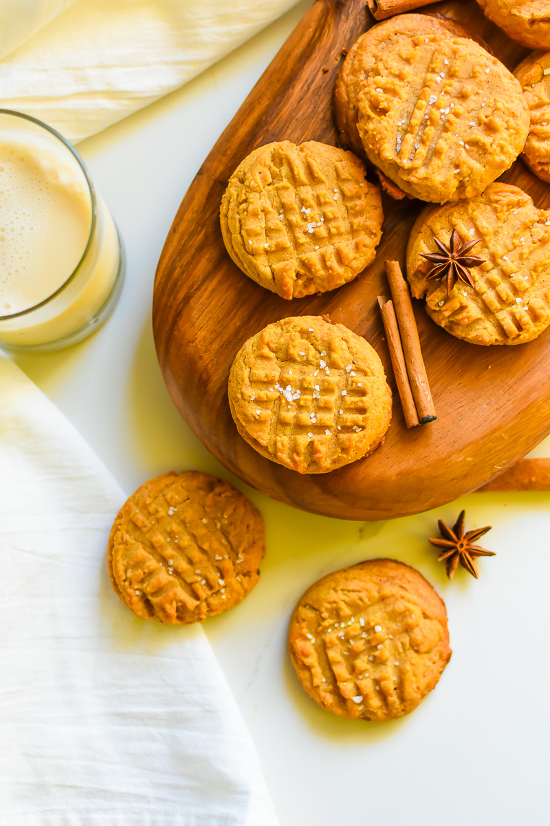 salted peanut butter cookies with chai spices on wooden serving board next to glass of milk.