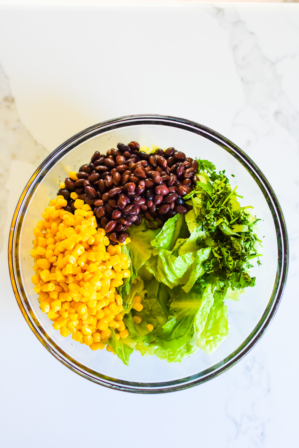 chopped romaine lettuce, corn, black beans, and cilantro in glass mixing bowl.