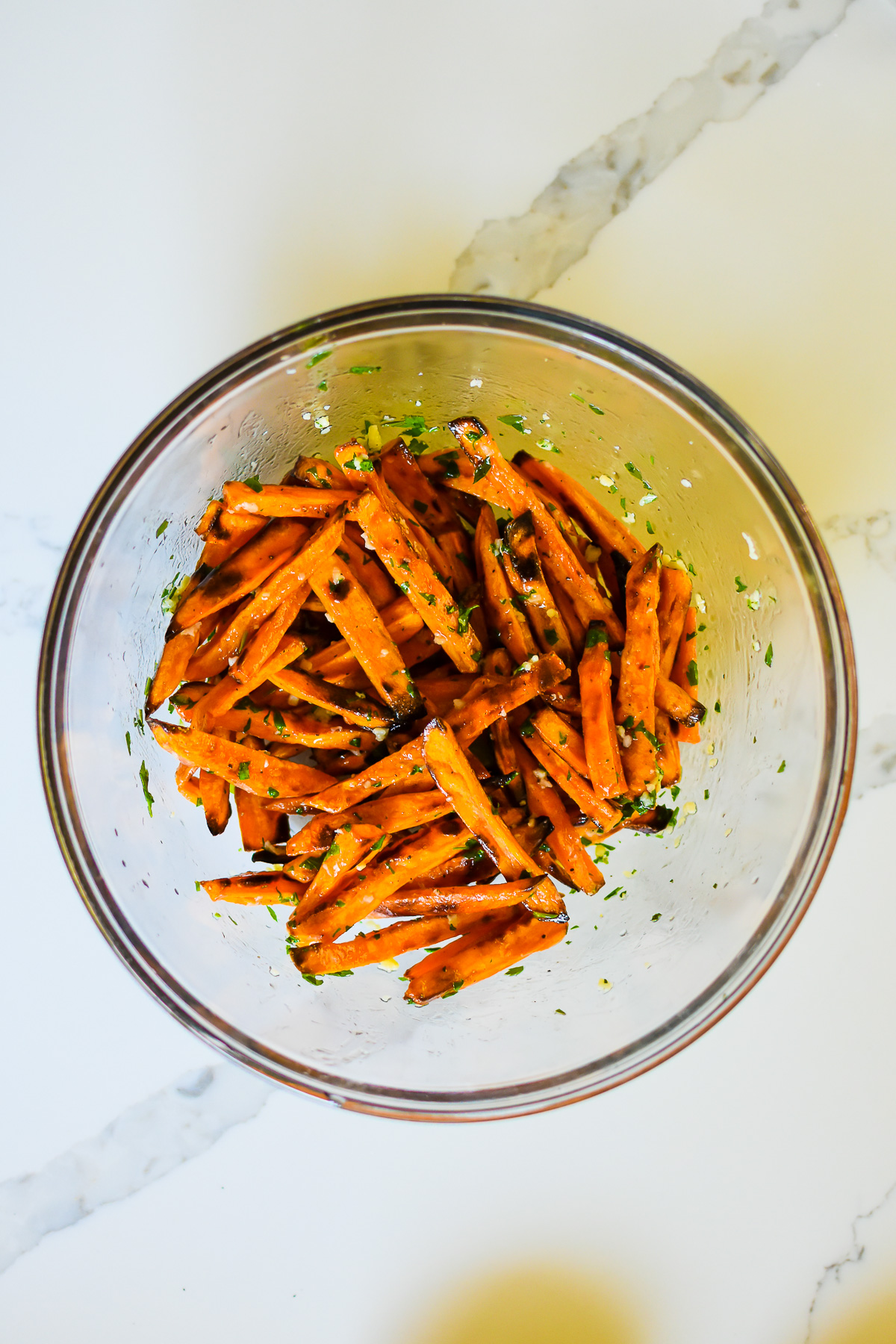 sweet potato fries tossed in garlic herb butter in glass mixing bowl.