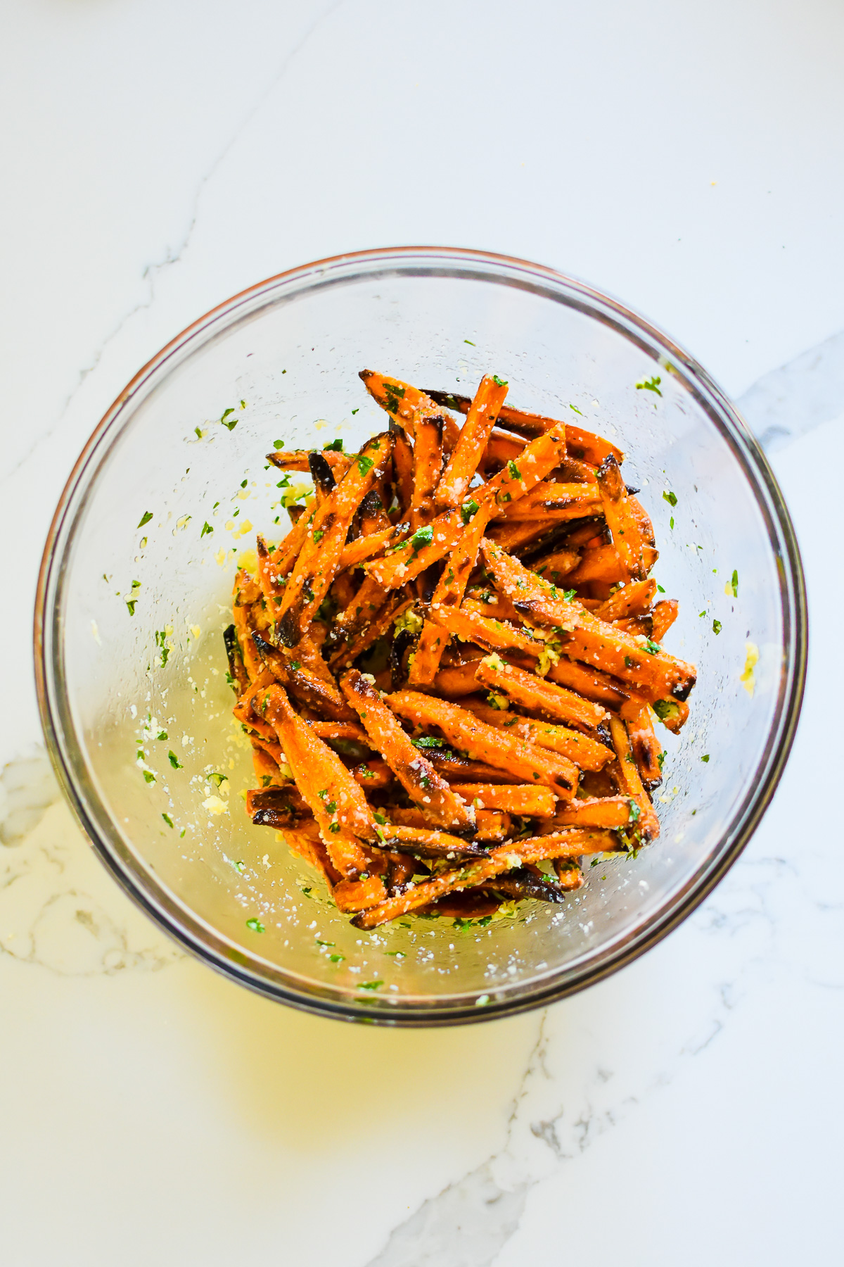 sweet potato fries tossed in garlic herb butter and parmesan cheese in glass mixing bowl.