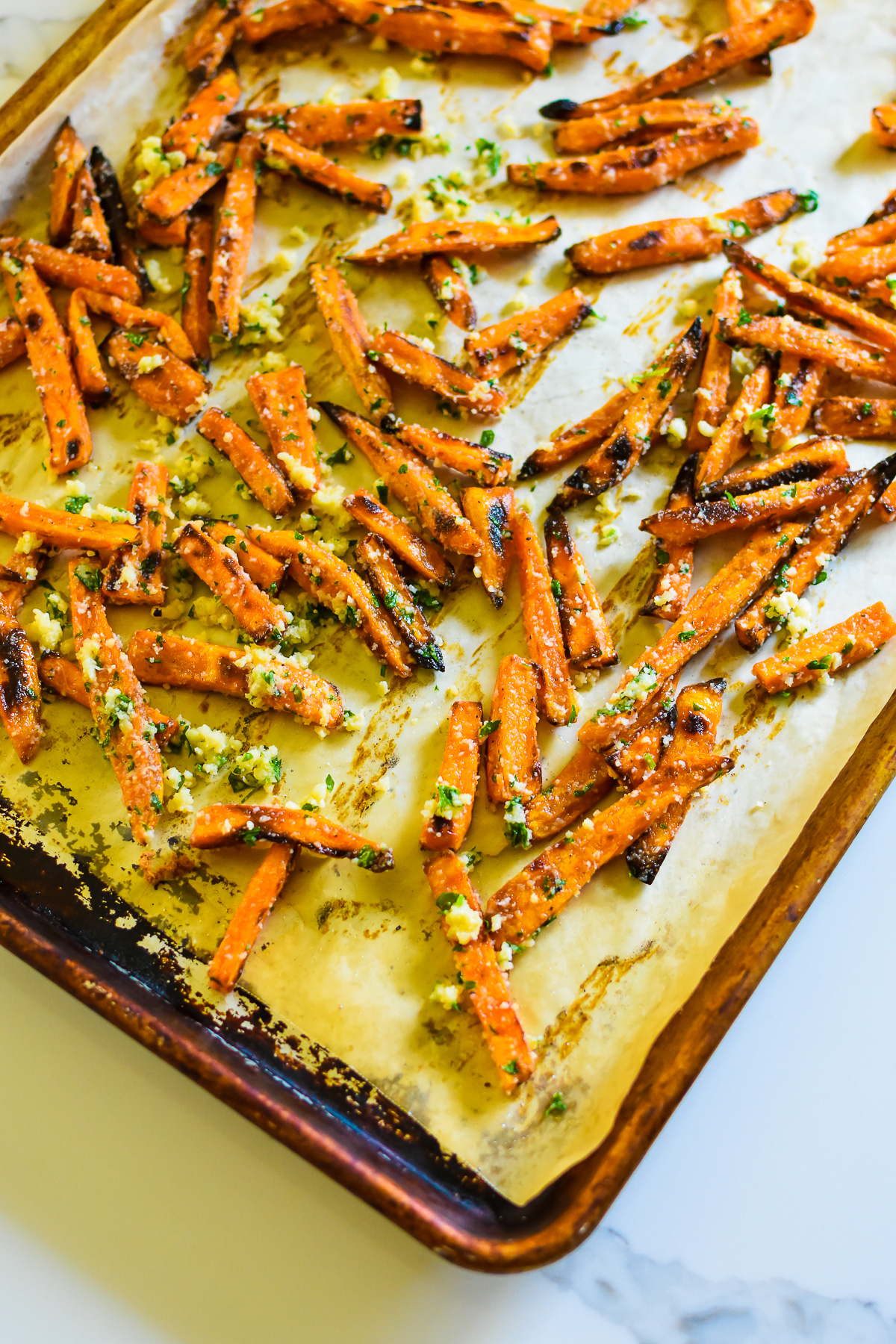 crispy homemade sweet potato fries on sheet pan tossed in garlic herb butter and parmesan cheese.