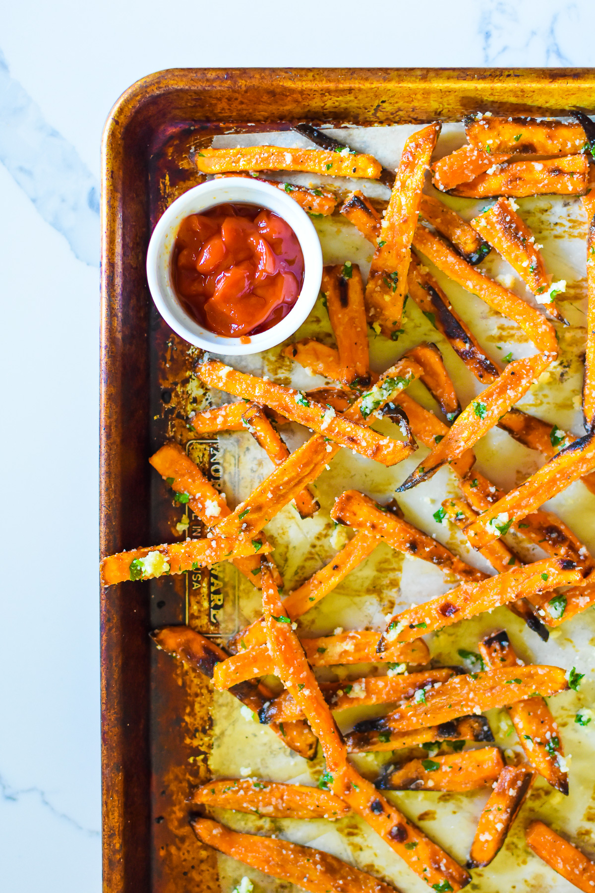 the best crispy baked sweet potato fries tossed with garlic herb butter on sheet pan with ramekin of ketchup.