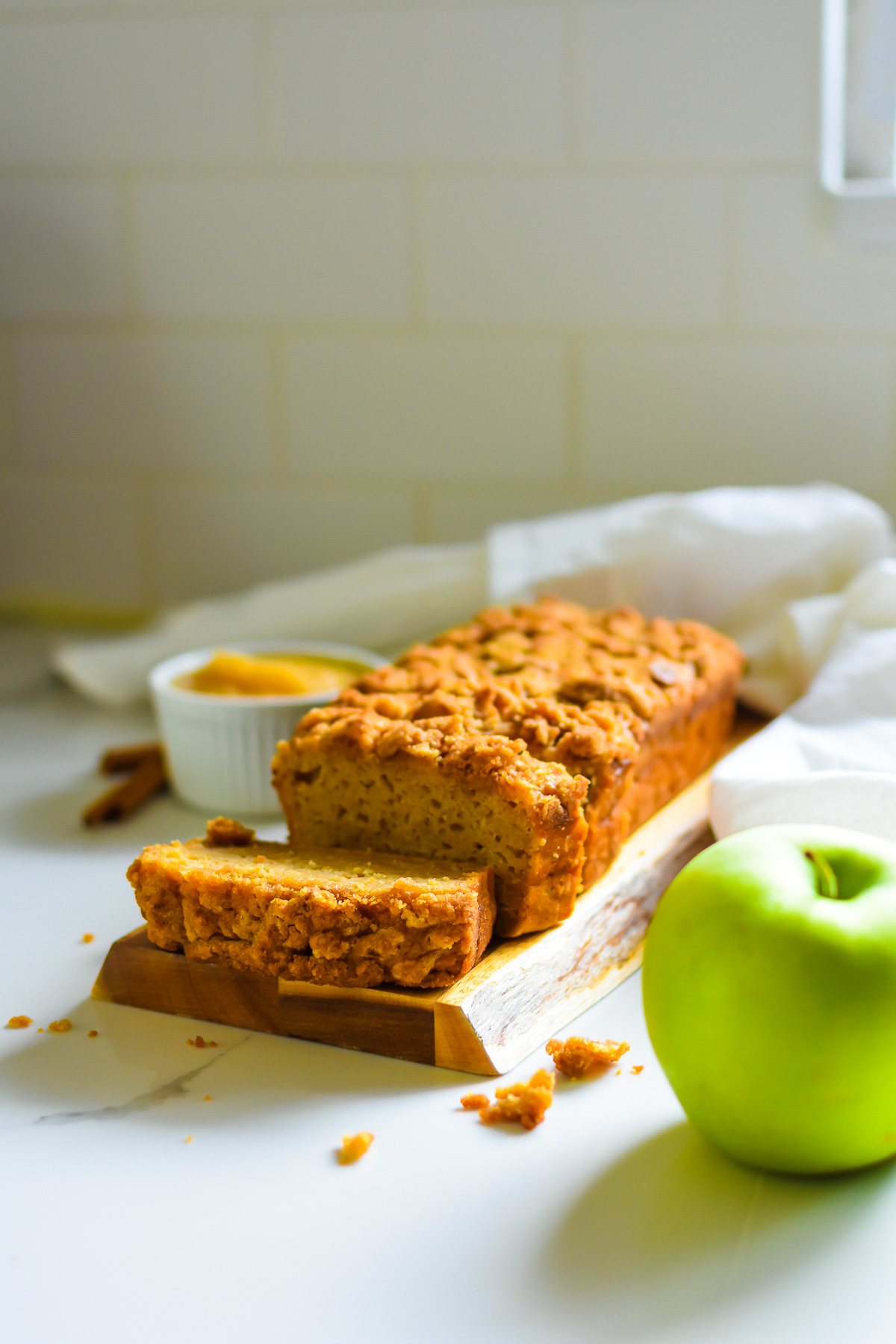 slices of the best spiced applesauce bread with crunchy brown sugar topping next to bowl of applesauce, cinnamon sticks, and Granny Smith apple.