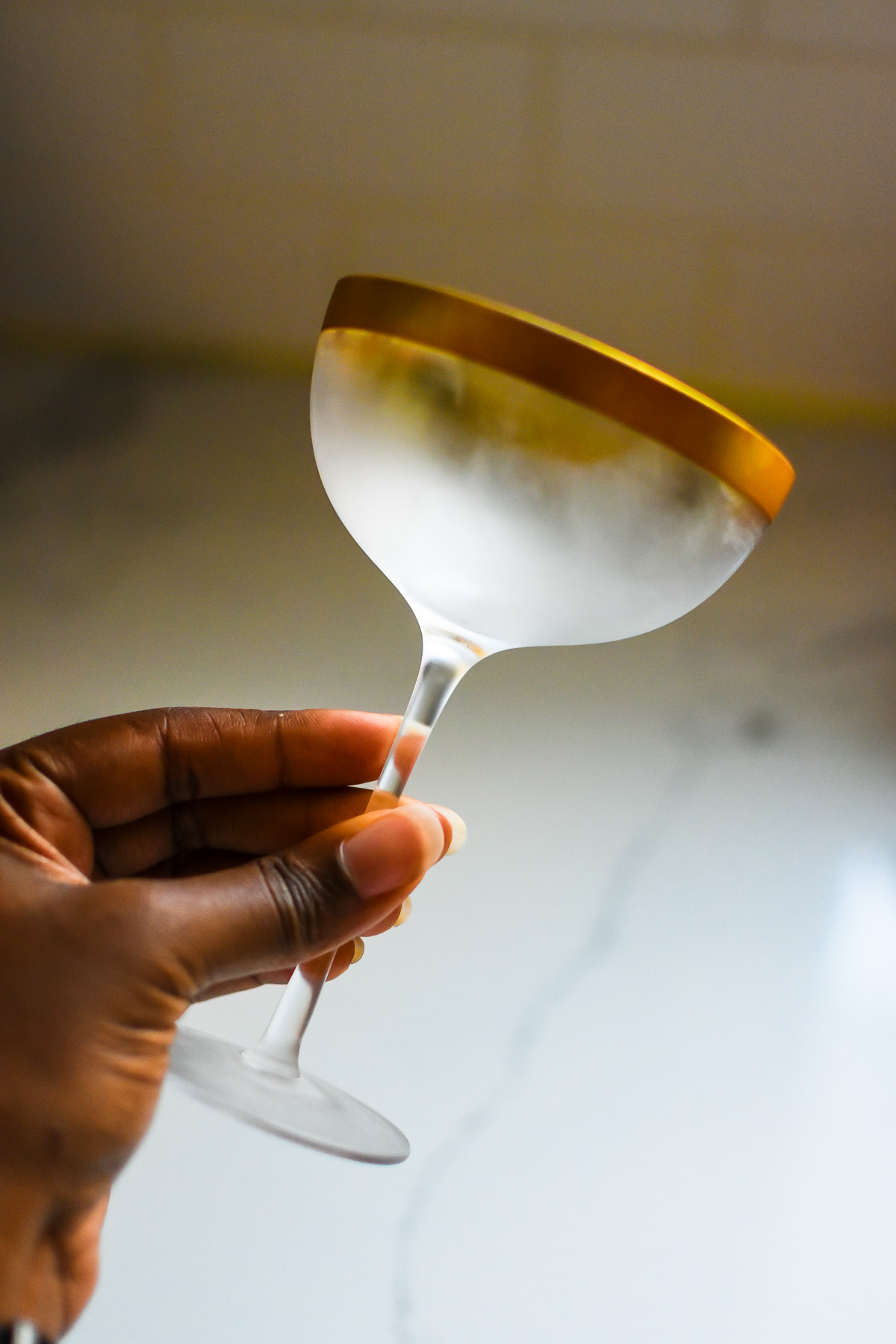 holding chilled and frosted coupe glass with gold rim.