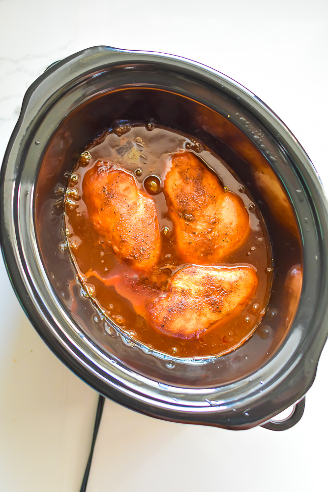 slow cooked chicken breast in bubbling barbecue sauce in crock pot.
