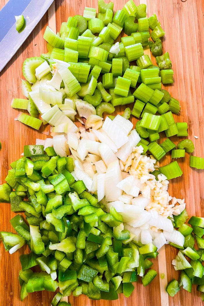 chopped celery, onion, bell pepper, and garlic on wooden cutting board.