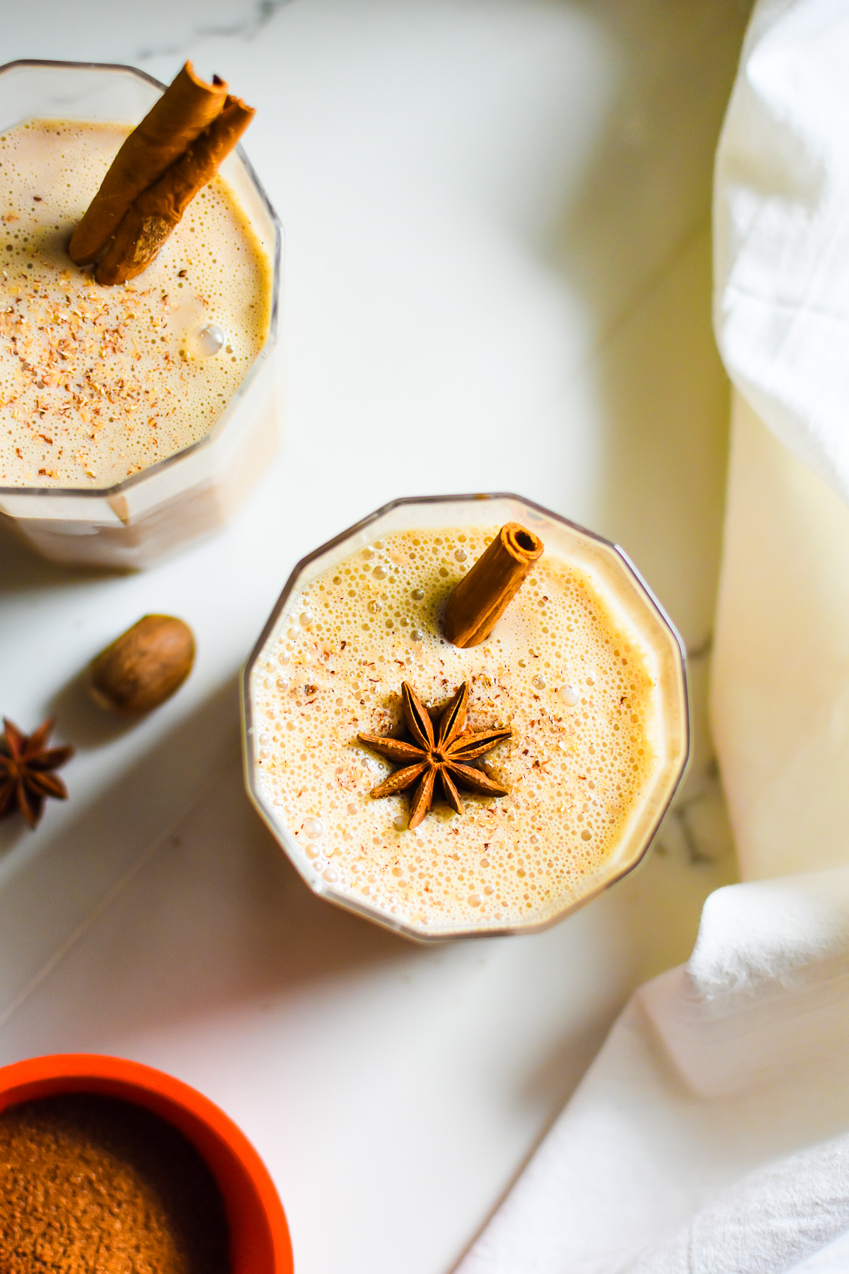 two glasses of homemade eggnog with chai spices garnished with nutmeg and cinnamon.