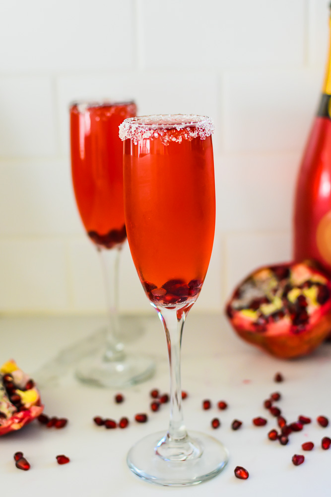 two pomegranate champagne cocktails garnished with pomegranate arils and a sparkling sugar rim.