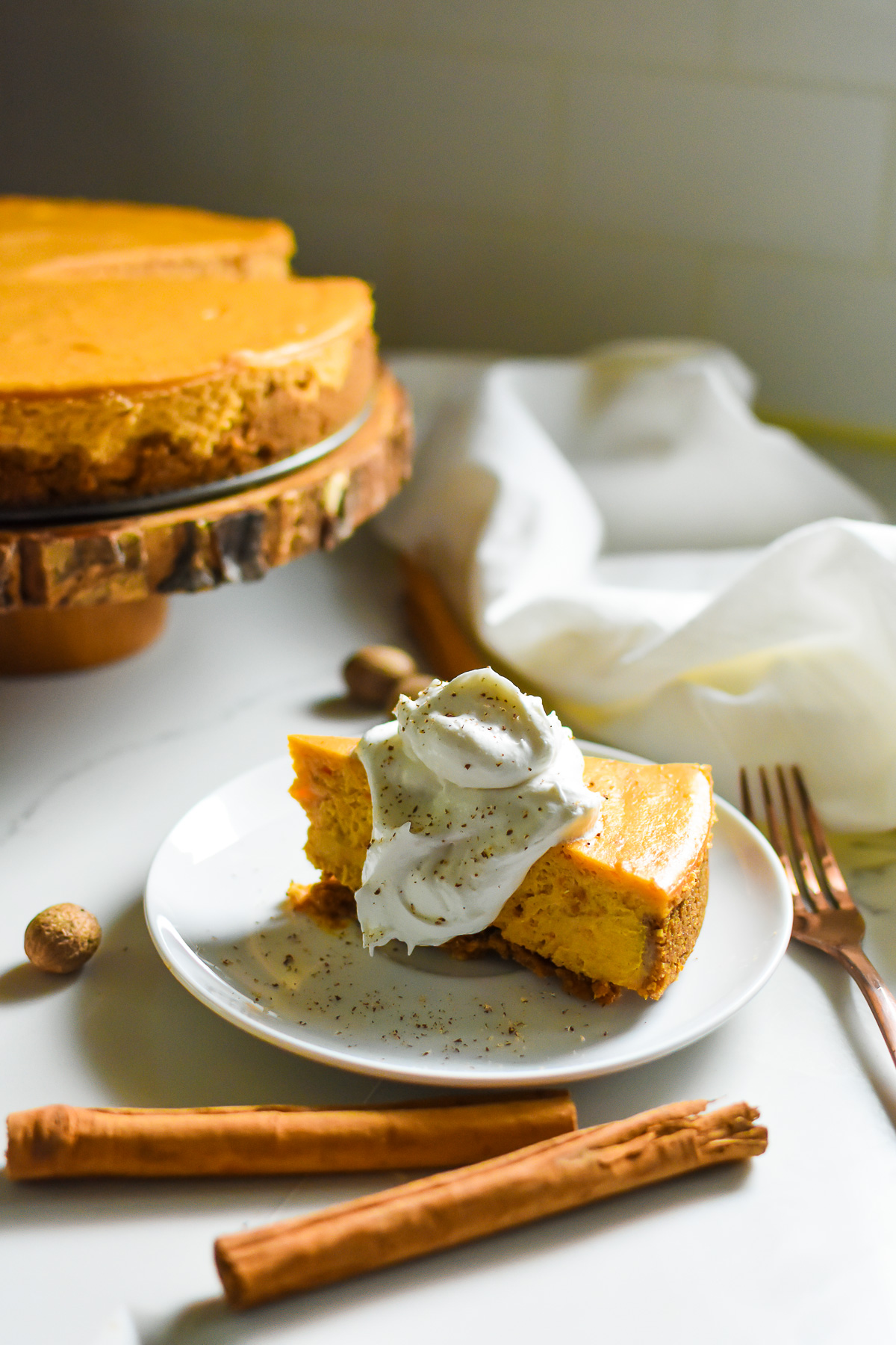slice of the best sweet potato pie cheesecake with spiced graham crust on white plate garnished with whipped cream and freshly grated nutmeg.